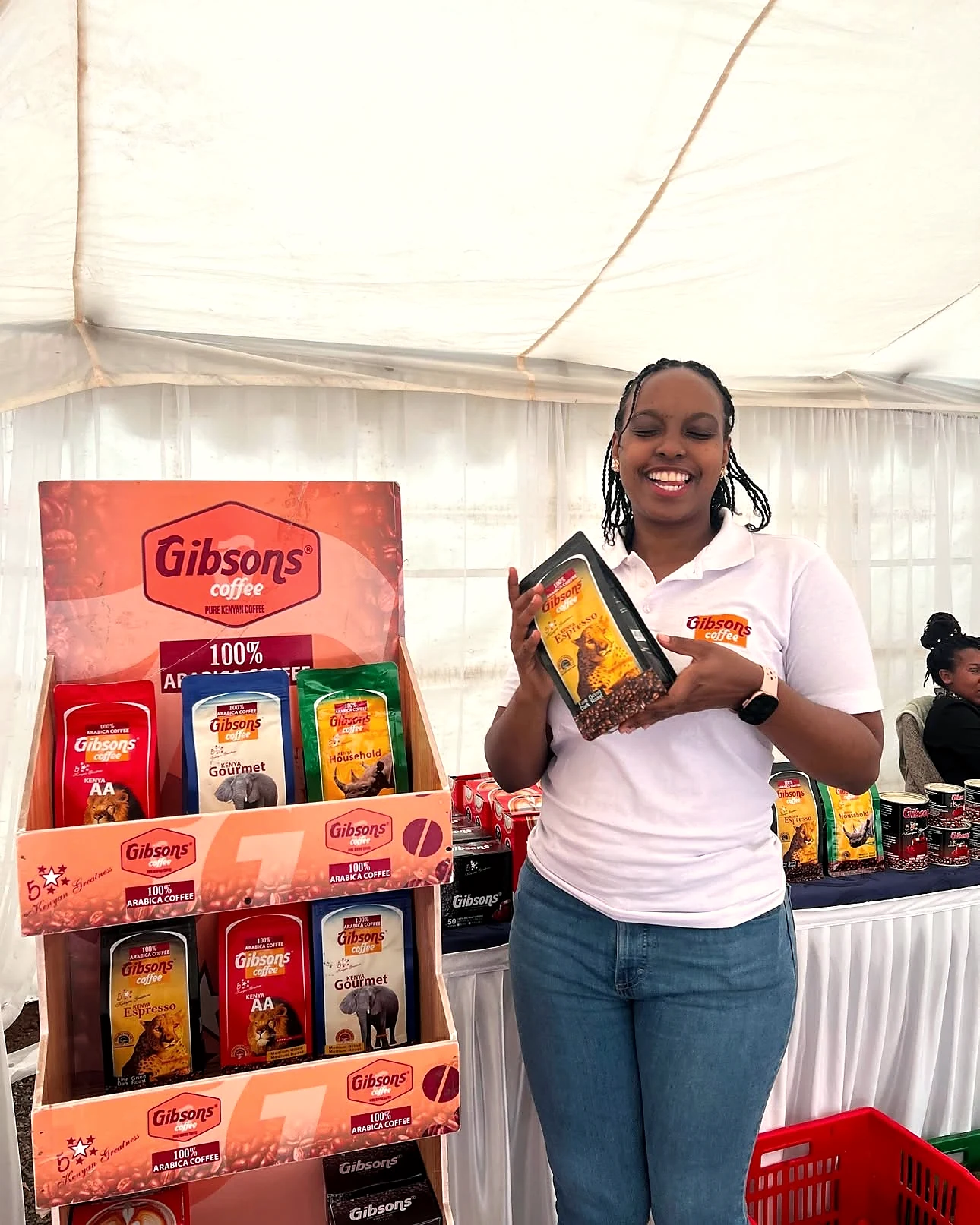 A smiling Gibsons Coffee team member presenting Kenya Espresso beside the coffee display