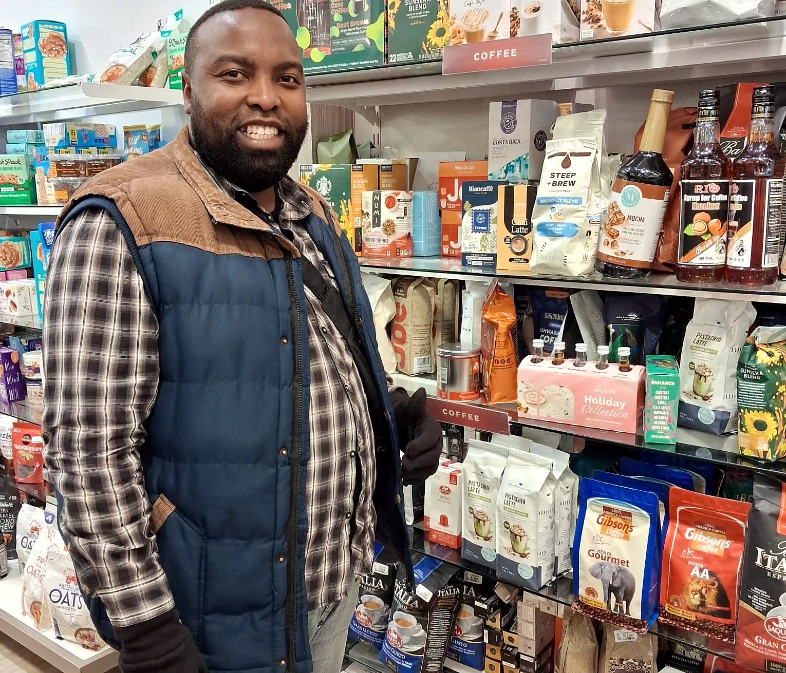 A smiling coffee enthusiast beside Gibsons coffee packs on USA retail shelves